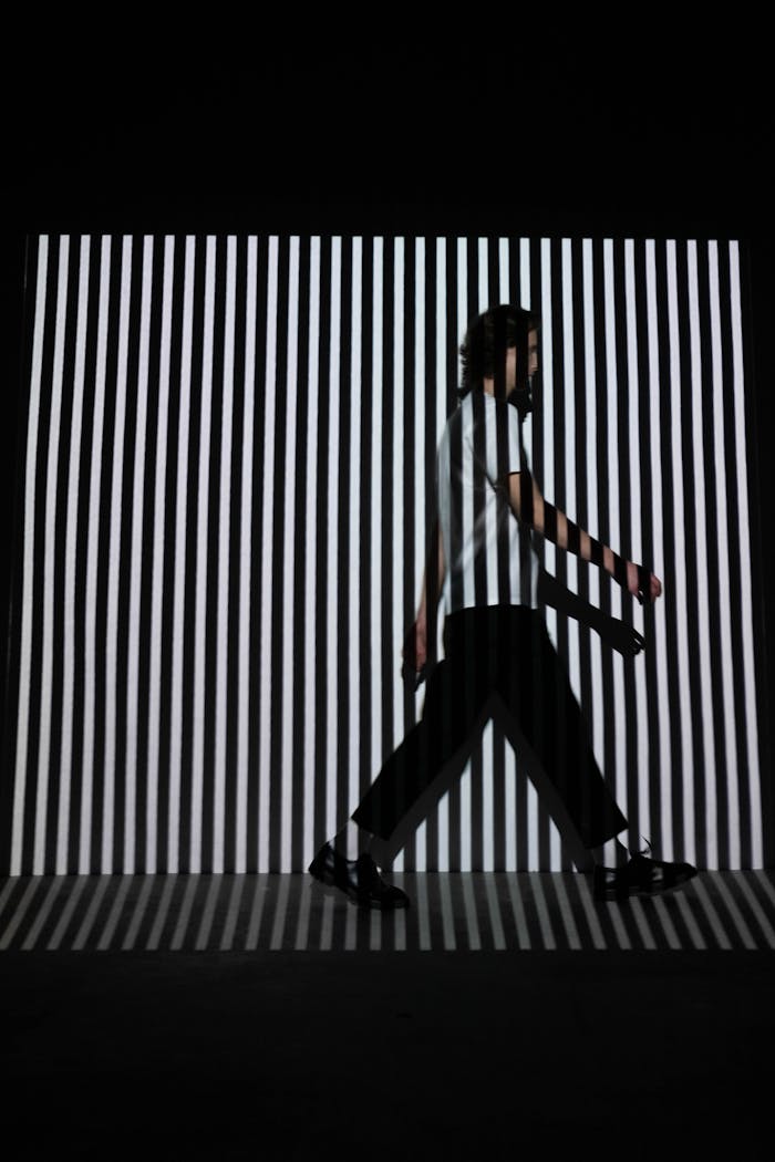 A man walks in front of a black and white striped optical illusion background.